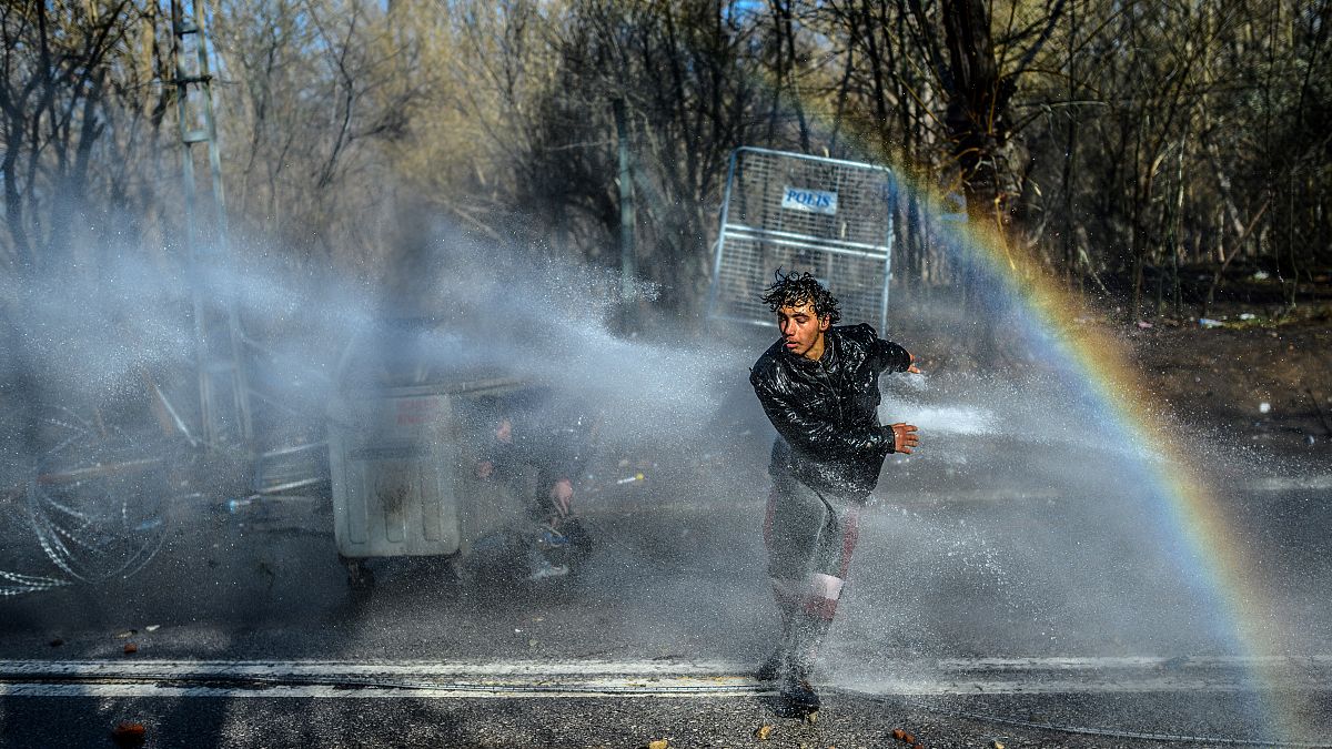 Un migrante huye mientras la policía griega utiliza cañones de agua para bloquearlo intentando romper las vallas en la frontera turco-griega de Edirne