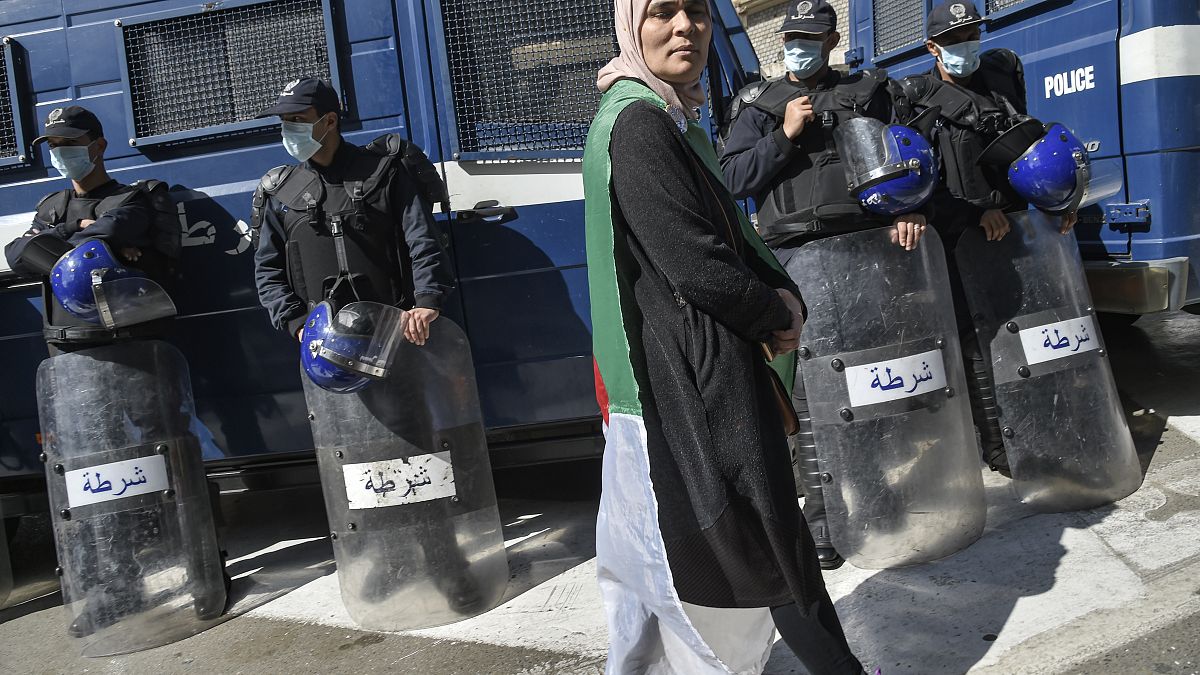 متظاهرة جزائرية تسير أمام أفراد الشرطة الذين وضعوا كمامات واقية خلال الحراك الأسبوعي بالعاصمة الجزائر. 06/03/2020
