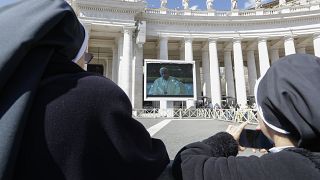 Nuns watch Pope Francis on a giant screen as he delivers the Angelus, in St. Peter's Square, at the Vatican, Sunday, March 8, 2020.