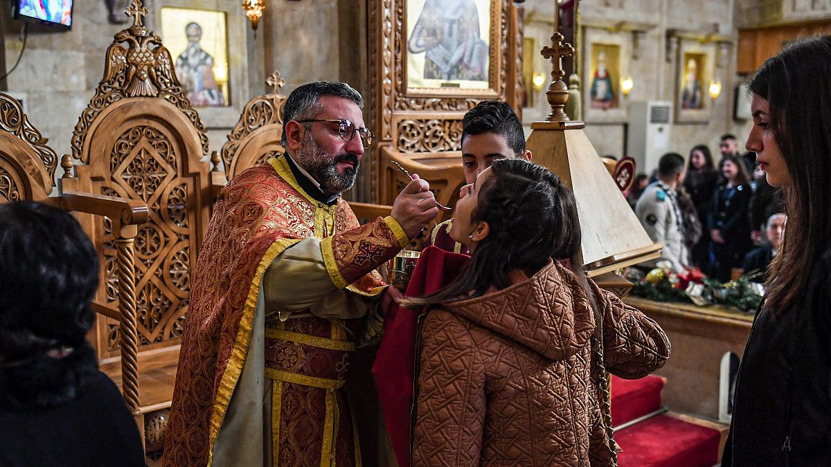 Fedeli ricevono la comunione con il rituale cucchiaino in una chiesa greca ortodossa siriana il 25 dicembre 2019 - AFP