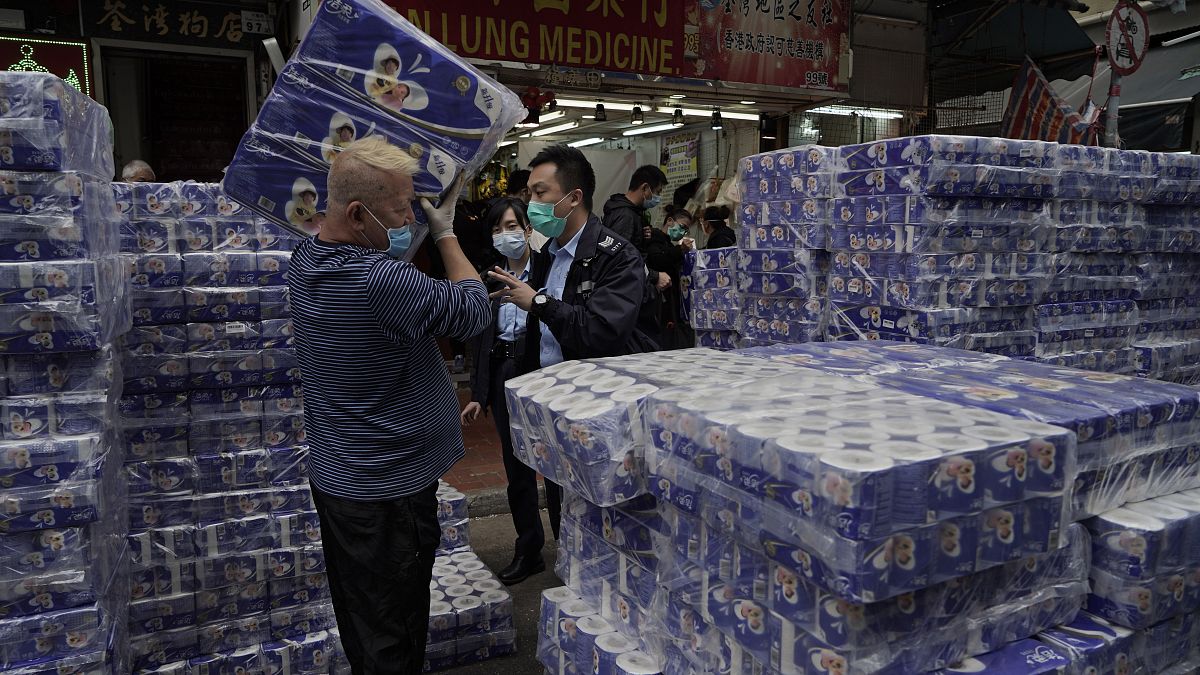 A shopkeeper, left, is questioned by police officers as packs of bath tissue papers block a road in Hong Kong, Saturday, Feb. 8, 2020. 
