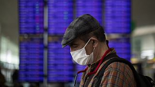 A man looks at his phone in front of the information screen at Barcelona airport, Spain, Thursday, March 12, 2020