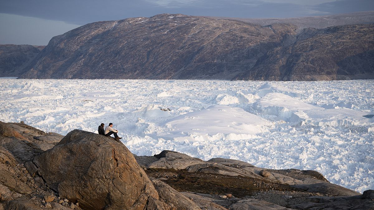 In this Aug. 16, 2019, file photo, NYU student researchers sit on top of a rock overlooking the Helheim glacier in Greenland. 
