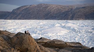 In this Aug. 16, 2019, file photo, NYU student researchers sit on top of a rock overlooking the Helheim glacier in Greenland.
