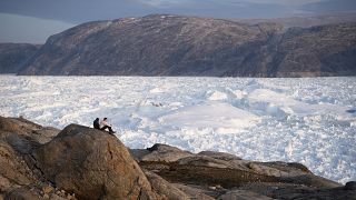 In this Aug. 16, 2019, file photo, NYU student researchers sit on top of a rock overlooking the Helheim glacier in Greenland. 