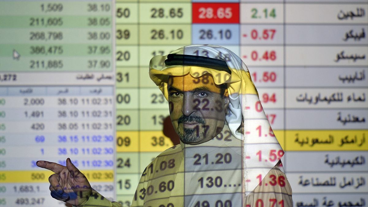 رجل أعمال سعودي يتحدث مع أخرين وخلفه شاشة كبيرة للسوق المالي في المصرف الوطني العربي بالعاصمة الرياض. 12/12/2019