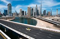 A lone taxi cab drives over a typically gridlocked highway with the Burj Khalifa, the world's tallest building, seen in the skyline behind it in Dubai, United Arab Emirates