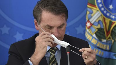 Brazil's President Jair Bolsonaro puts on a mask during a press conference on the new coronavirus at the Planalto Presidential Palace in Brasilia, Brazil, March 18, 2020