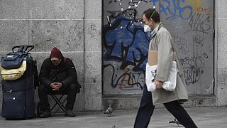 Un hombre protegido con una máscara pasea cerca de un 'sin techo' en Puerta del Sol, Madrid
