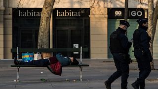 Policemen walks by a homeless man sleeping on a bench on March 17, 2020 in Paris