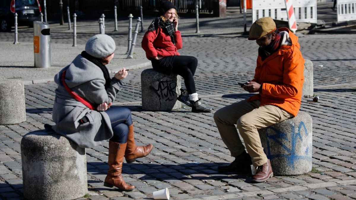 People sit on the bollards on the Admiral Bridge in Berlin's Kreuzberg district on March 22, 2020, amidst the new coronavirus COVID-19 pandemic. (Photo by David GANNON / AFP)