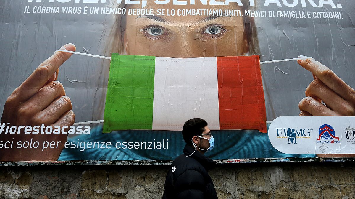 A man walks past a large billboard raising awareness to the measures taken by the Italian government to fight against the spread of the COVID-19.