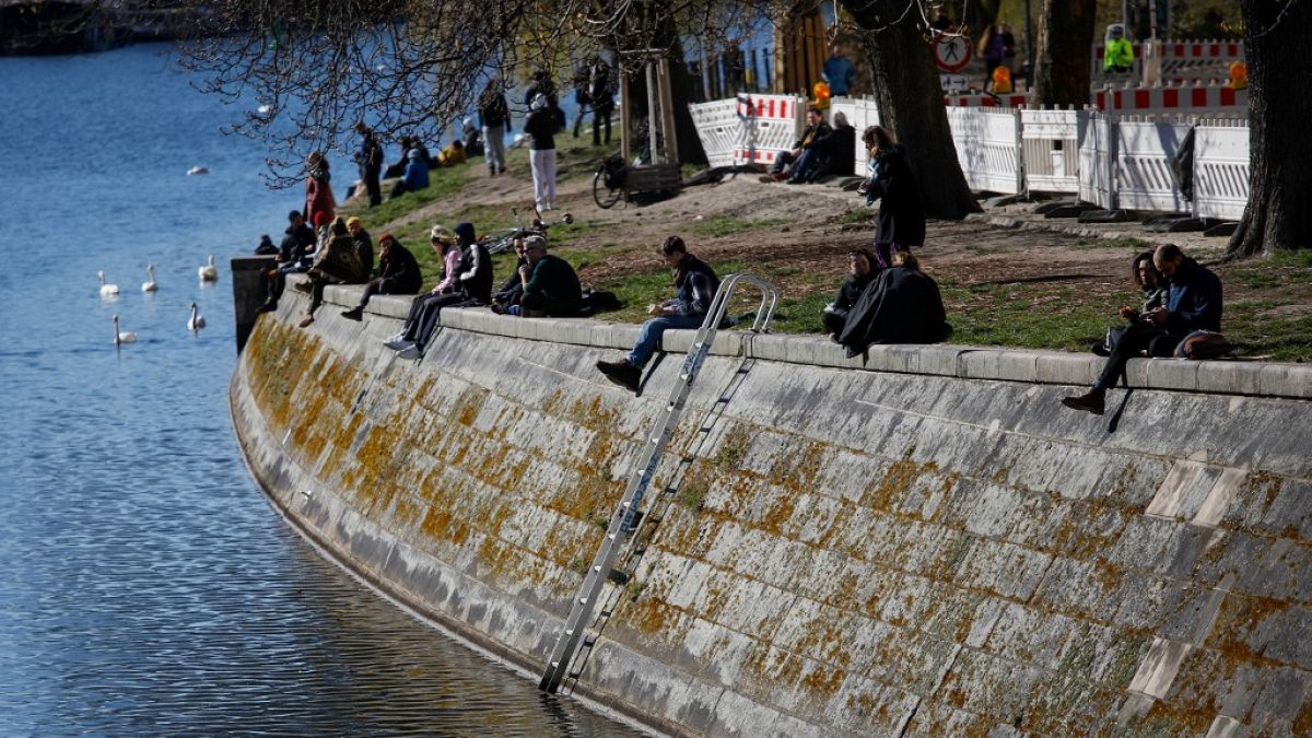 People sit in the sun on the banks of the Landwehr Canal in Berlin's Kreuzberg district on March 22, 2020,