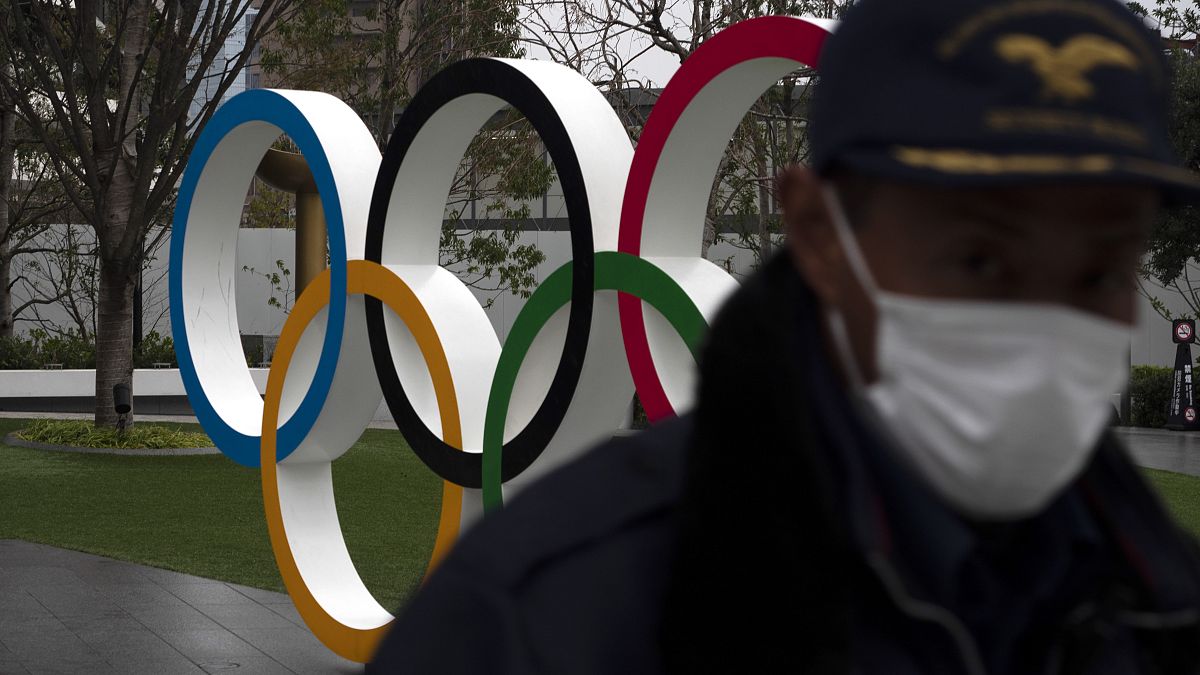 مواطن ياباني يقف امام شعار الالعاب الأولمبية في طوكيو - 2020/03/23