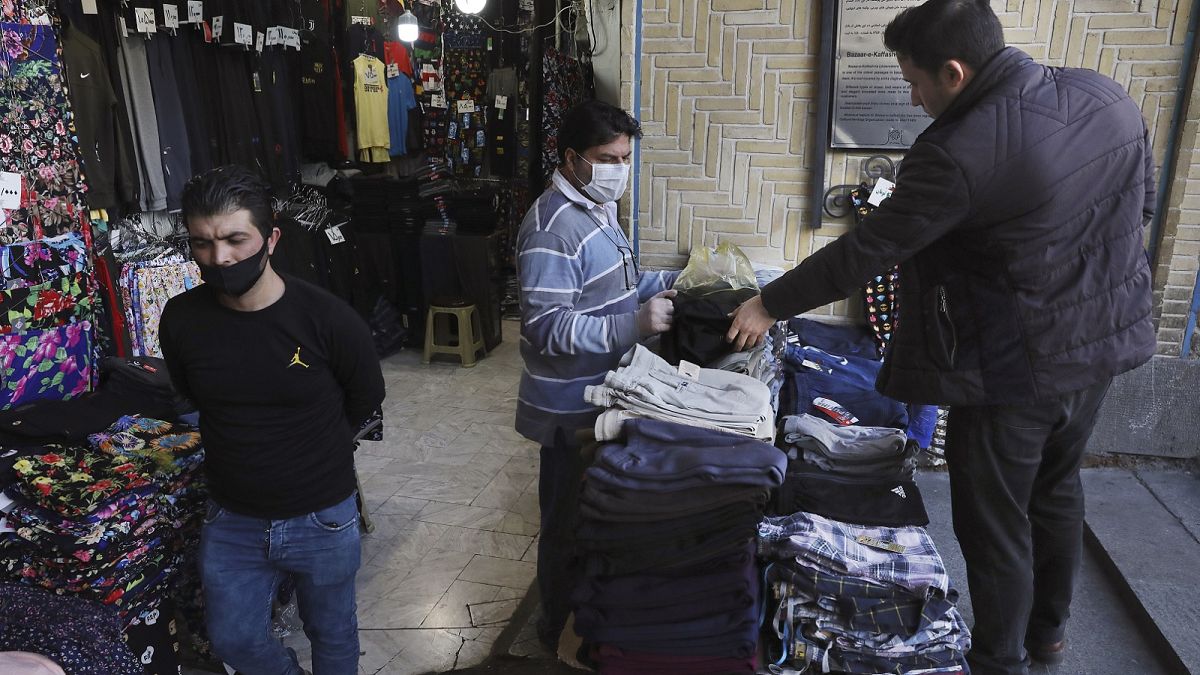A shopkeeper, center, wearing a face mask and gloves, to help protect against the new coronavirus, talks with his customer at the Tehran's Grand Bazaar, Iran