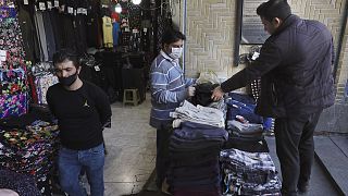 A shopkeeper, center, wearing a face mask and gloves, to help protect against the new coronavirus, talks with his customer at the Tehran's Grand Bazaar, Iran