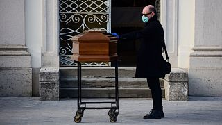 A man touches the coffin of his mother during a funeral service in the closed cemetery of Seriate, near Bergamo
