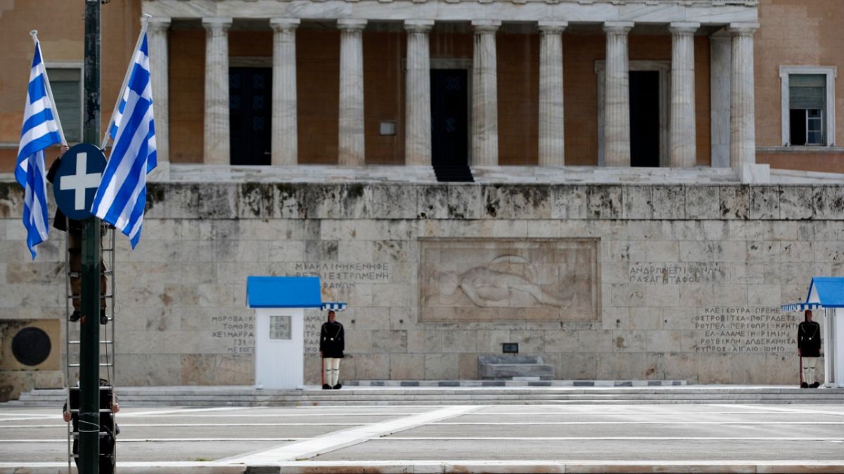 Municipal workers install Greek flags in front of the Greek parliament as Presidential guards are on duty at the empty Tomb of the Unknown Soldier Athens on March 24, 2020.