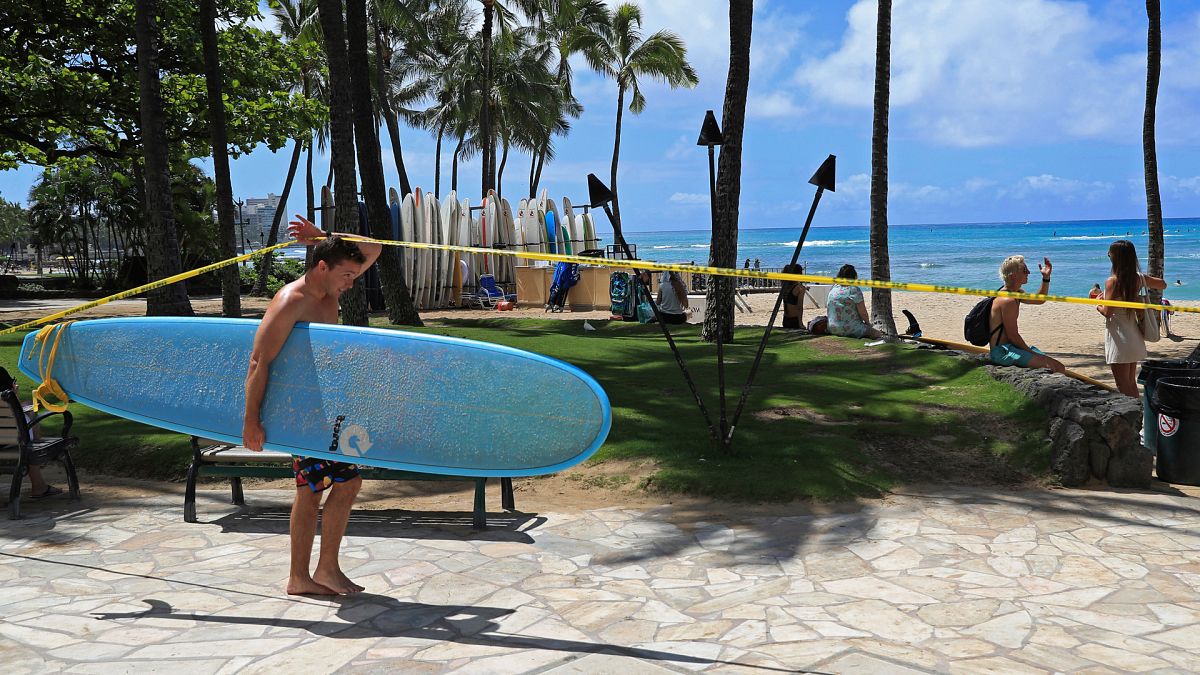 Un surfeur passe sous la ligne de signalisation à Waikiki, le vendredi 20 mars 2020, à Honolulu.