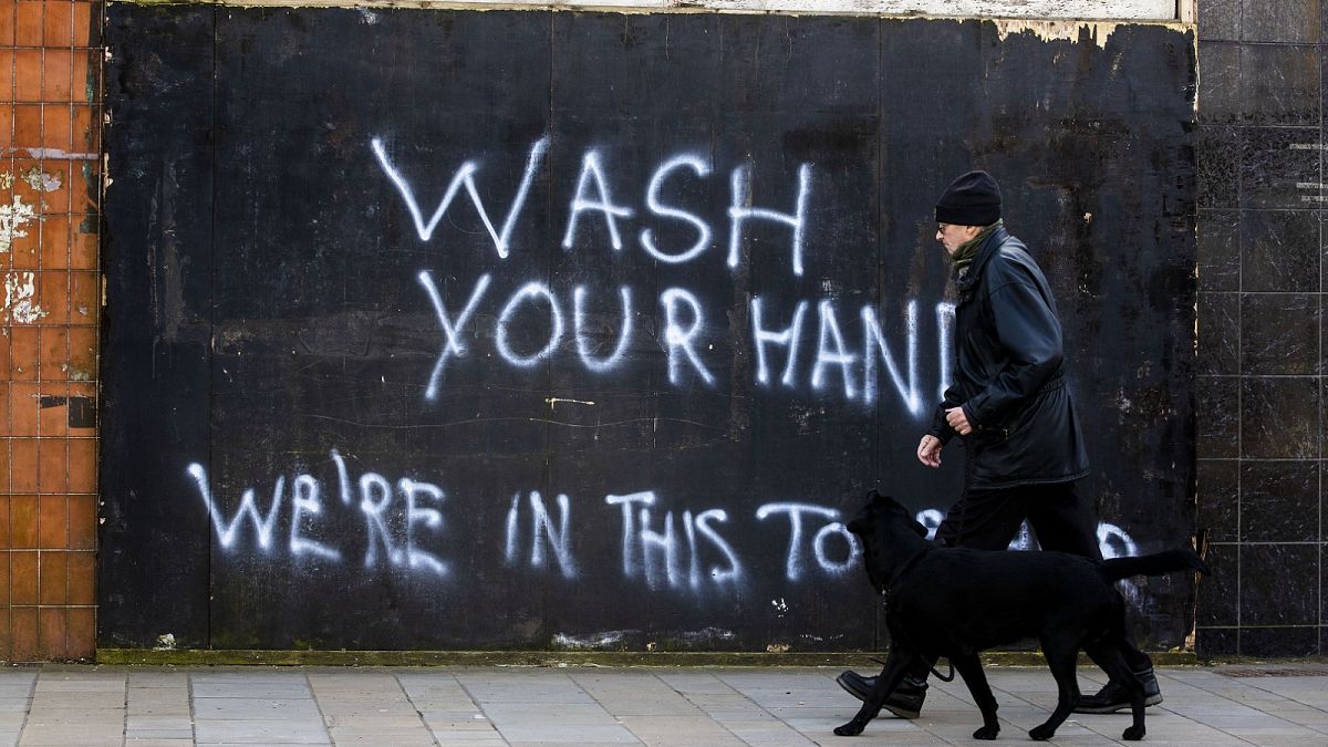 A man walking a dog past graffiti with the writing, "Wash Your Hands, We're In This Together", on the Lower Newtownards Road in Belfast, Tuesday March 24, 2020
