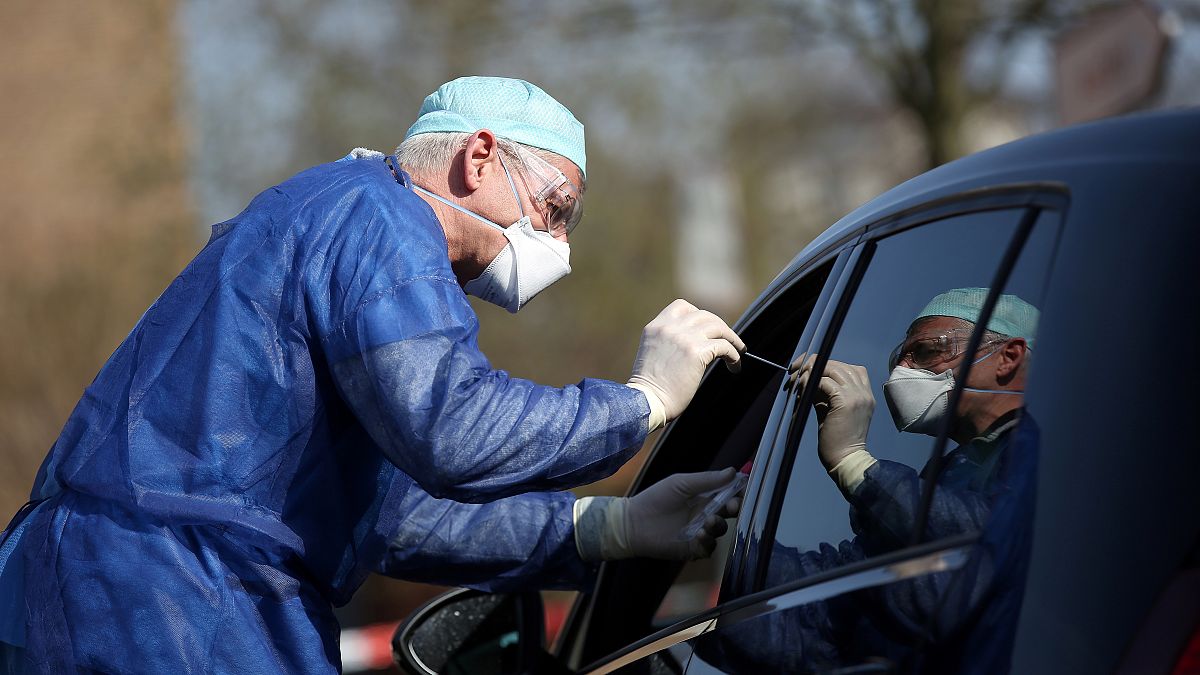 German doctor Michael Grosse swabs the throat of a car driver through the window on March 27, 2020 at a drive through testing point in Halle, eastern Germany.