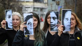 Women's rights activists hold printed half face pictures showing victims of domestic violence during a protest in Bucharest on March 4, 2020