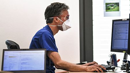A doctor with a face mask to protect from COVID-19 works in his office on a computer in Essen, Germany, 2020.