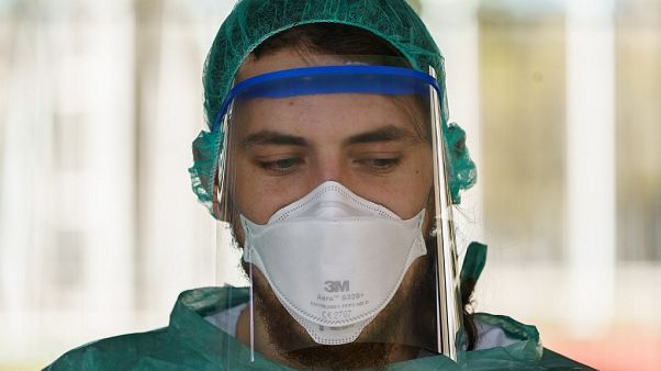 A healthcare worker dressed in protective gear waits for drivers at a drive-through testing. (Photo by CESAR MANSO / AFP) A healthcare worker dressed in protective gear waits for drivers at a drive-through testing. (Photo by CESAR MANSO / AFP)