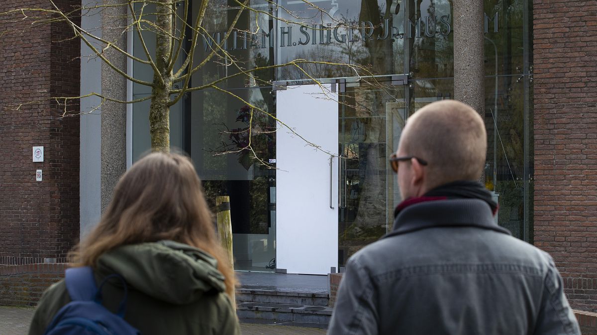 Two people look at the glass door which was smashed during a break-in at the Singer Museum in Laren, Netherlands, Monday March 30, 2020. 