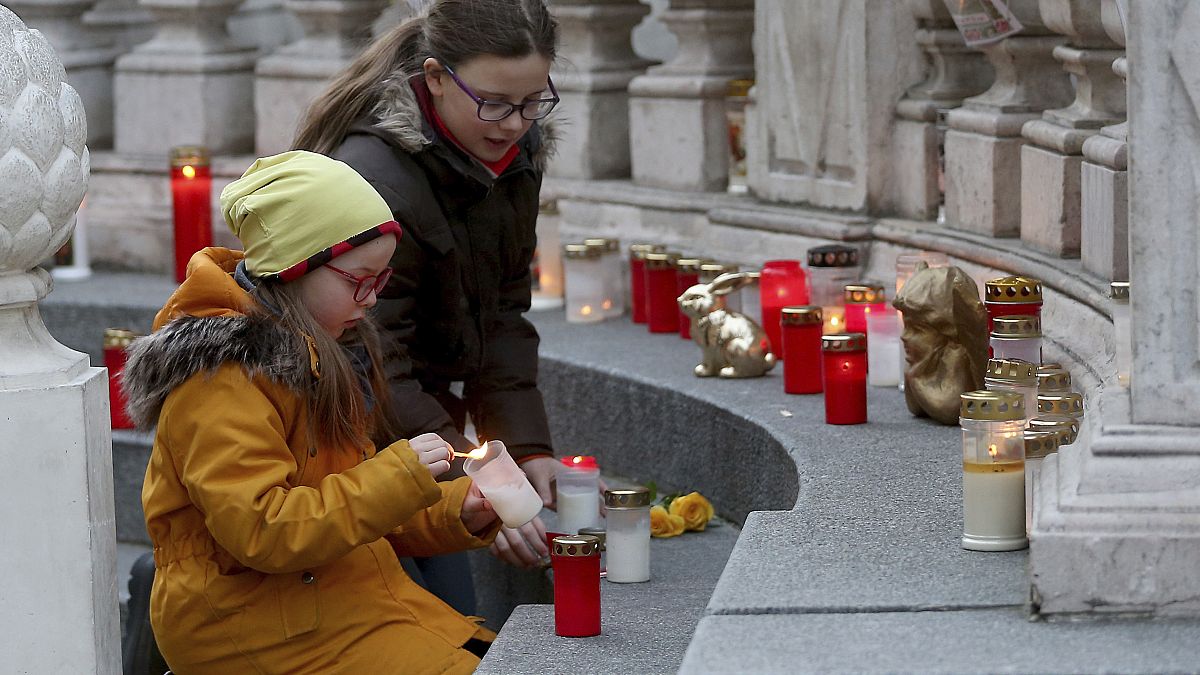 Two girls light candles in front of the plague column in Vienna, Austria, Thursday, March 26, 2020. 