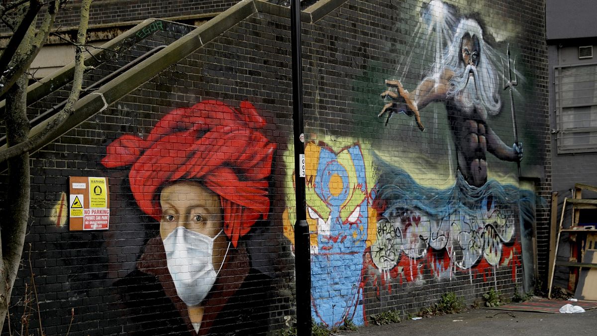 A mural by street artist Lionel Stanhope with a face mask reference to coronavirus next to one of his other works, at right, painted on a bridge wall in Ladywell