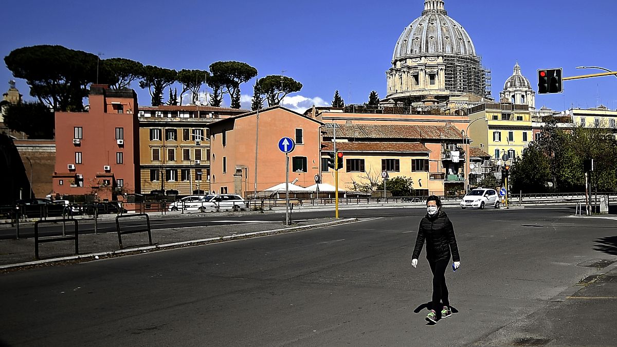 A woman walks with St Peter's Basilica in the background in Rome on April 6, 2020
