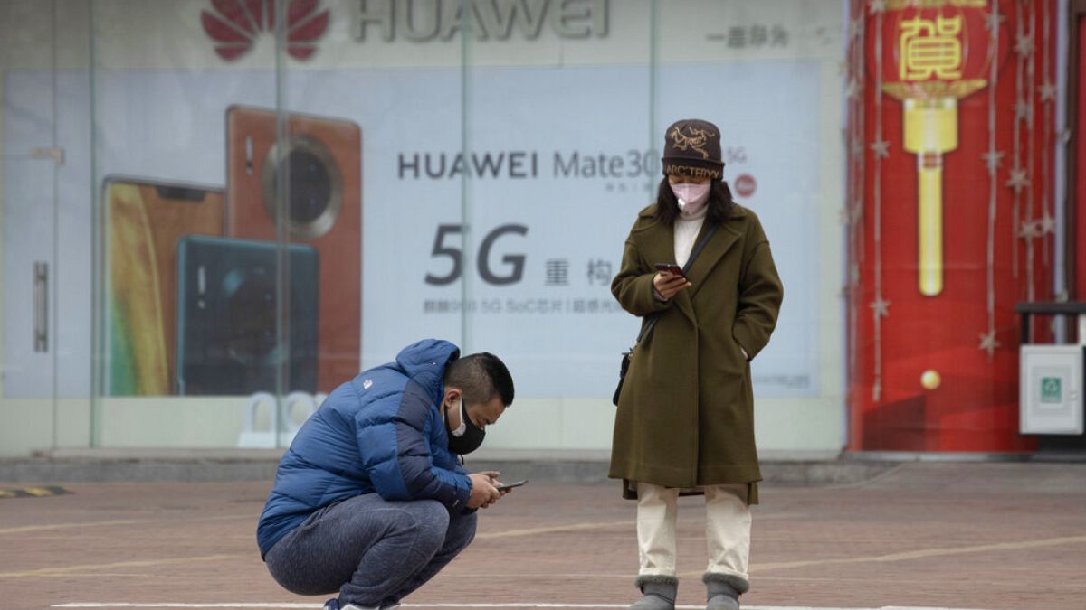 Dos personas mirando sus teléfonos en Pekín frente a una publicidad de 5G
