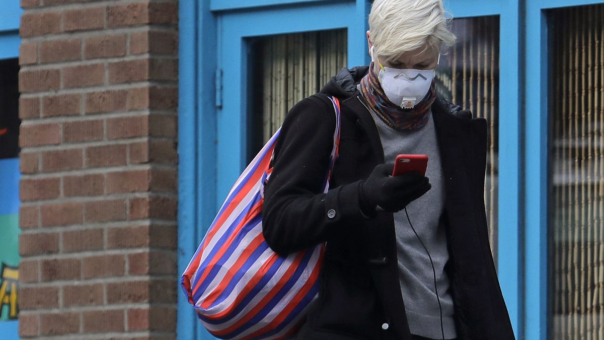 Une femme porte un masque et consulte son téléphone, le mardi 24 mars 2020, dans le quartier de Capitol Hill à Seattle.