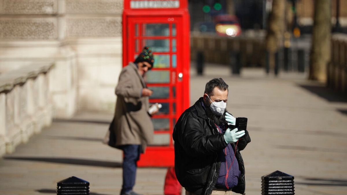 A man wearing a mask looks at his phone near Parliament Square, in London, Wednesday, March 25, 2020.