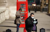 A man wearing a mask looks at his phone near Parliament Square, in London, Wednesday, March 25, 2020.