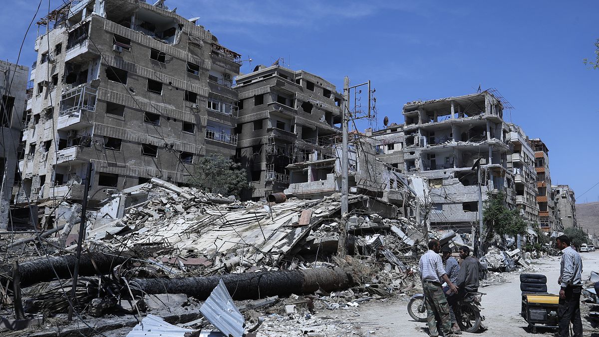 In this Monday, April 16, 2018 file photo, people stand in front of damaged buildings, in the town of Douma, the site of a suspected chemical weapons attack.