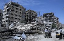 أشخاص يقفون أمام مبان مدمرة في بلدة دوما، موقع هجوم بالأسلحة الكيماوية بالقرب من دمشق ، سوريا. 2018/04/16