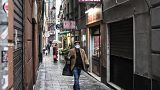 A resident wearing a protection mask carrying a shopping bag walks past shops as they close up under the lockdown in Genoa, Italy, March 13, 2020.