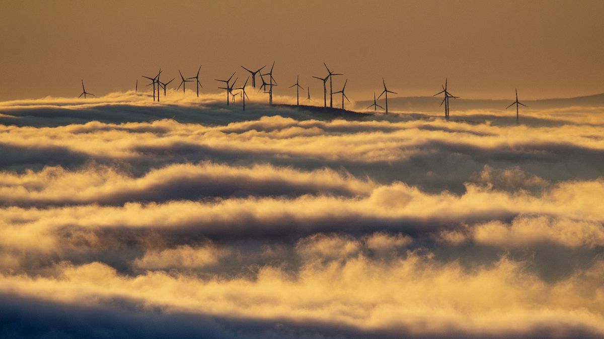 Wind turbines stand on a hill and are surrounded by fog and clouds in the Taunus region near Frankfurt, Germany