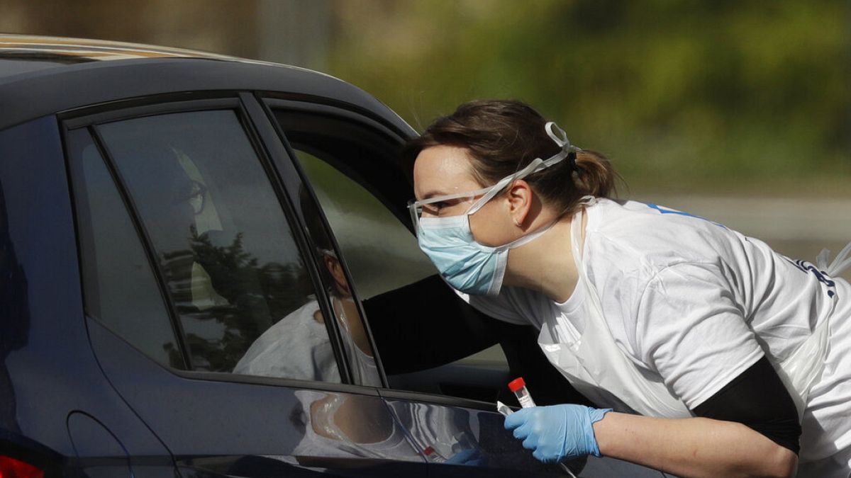 Egy egészségügyi dolgozó koronavírusteszthez vesz mintát egy autóstól