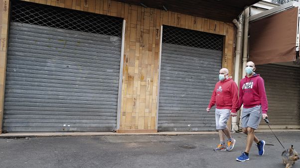 A couple wearing protective masks walks their dog front of a closed shop during a nationwide confinement to counter the COVID-19, in Paris Sunday April 12, 2020. 