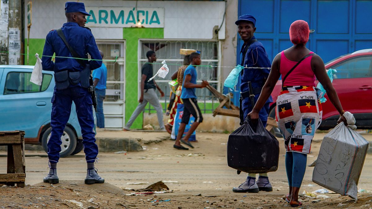 A saleswoman tries to pass the prohibited sale zone as two police officers look an at the Avo Kumbi sqaure in Luanda, Angola, on April 2, 2020.