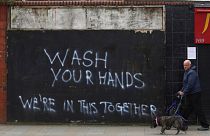 A man walks his dog past graffiti calling for people to wash their hands to combat the spread of the coronavirus, in Belfast, Northern Ireland, Monday March, 30, 2020