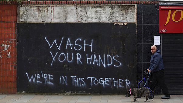 A man walks his dog past graffiti calling for people to wash their hands to combat the spread of the coronavirus, in Belfast, Northern Ireland, Monday March, 30, 2020 A man walks his dog past graffiti calling for people to wash their hands to combat the spread of the coronavirus, in Belfast, Northern Ireland, Monday March, 30, 2020