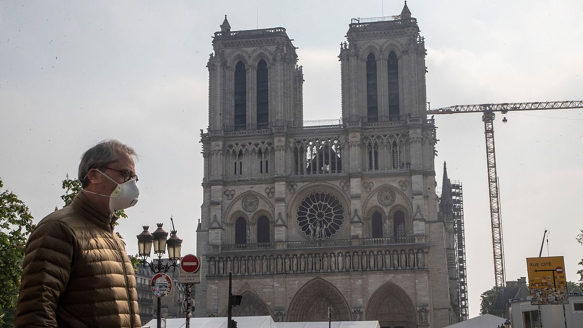 A man in a mask walks past Notre Dame Cathedral in Paris