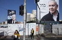 In this March. 1, 2020 file photo, people walk next to election campaign billboards showing Israeli Prime Minister Benjamin Netanyahu, right, and Benny Gantz, left, in Bnei Br