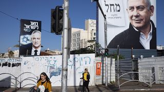 In this March. 1, 2020 file photo, people walk next to election campaign billboards showing Israeli Prime Minister Benjamin Netanyahu, right, and Benny Gantz, left, in Bnei Br