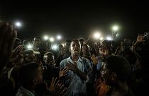 People chant slogans as a young man recites a poem, illuminated by mobile phones, before the opposition's direct dialogue with people in Khartoum on June 19, 2019