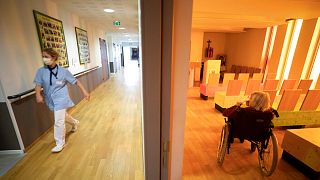 A nurse walks in a corridor of a nursing home as a resident sits in a chapel during a COVID-19 testing session in Bergheim, eastern France, Tuesday April 14, 2020